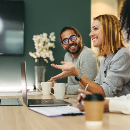 Business woman talking to her colleagues during a meeting in a boardroom. Group of happy business people working together in a creative office.